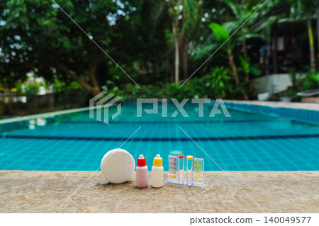 Pool water testing kit and chlorine tablet with reagent bottles on stone edge, clean blue swimming pool background Pool water testing kit and chlorine tablet with reagent bottles on stone edge, clean blue swimming pool background 140049577