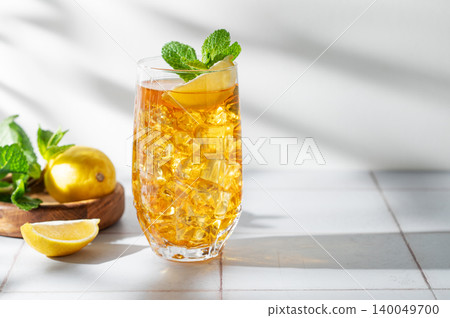 Iced tea with lemon and mint in a glass on a light tile background with shadows Iced tea with lemon and mint in a glass on a light tile background with shadows 140049700