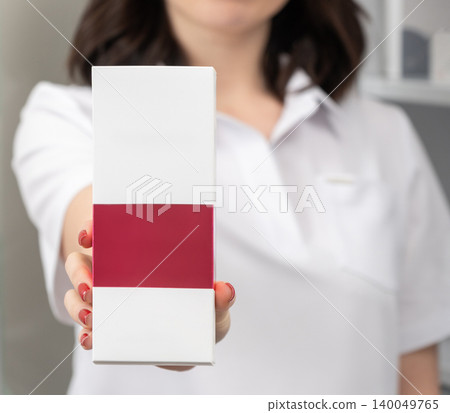 Woman in a white uniform holding a blank cosmetic product box Woman in a white uniform holding a blank cosmetic product box 140049765