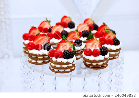 Desserts decorated with strawberries, raspberries, blackberries are arranged on clear stand for special event. Desserts decorated with strawberries, raspberries, blackberries are arranged on clear stand for special event. 140049858
