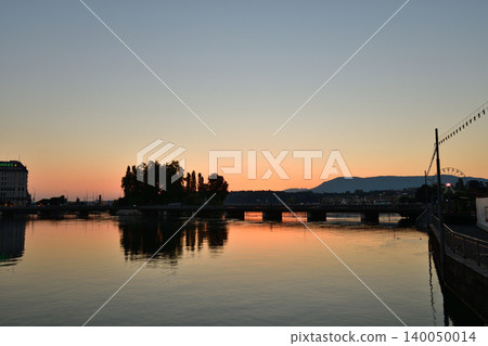 Sunrise over Lake Geneva, viewed from the Rhone River in Geneva. Swiss landscape (August 16, 2022) Sunrise over Lake Geneva, viewed from the Rhone River in Geneva. Swiss landscape (August 16, 2022) 140050014