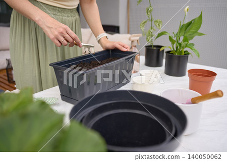 Woman prepares soil in planter box with hand tool on an outdoor gardening table Woman prepares soil in planter box with hand tool on an outdoor gardening table 140050062
