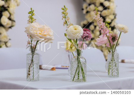 Vases filled with white pink flowers sit on wedding table at decorated event space with floral backdrop. Vases filled with white pink flowers sit on wedding table at decorated event space with floral backdrop. 140050103
