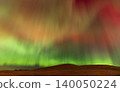 Vibrant aurora borealis dances across the night sky above rolling hills 140050224