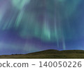 Vibrant aurora borealis dances across the starry night sky above a grassy hill 140050226