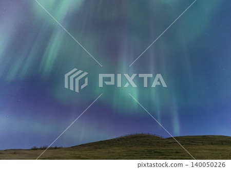 Vibrant aurora borealis dances across the starry night sky above a grassy hill Vibrant aurora borealis dances across the starry night sky above a grassy hill 140050226