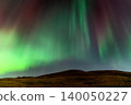 Vibrant green and red aurora borealis dances across a starry night sky over a hill 140050227