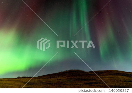 Vibrant green and red aurora borealis dances across a starry night sky over a hill Vibrant green and red aurora borealis dances across a starry night sky over a hill 140050227