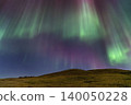 Vibrant aurora borealis dances across the night sky over rolling hills 140050228