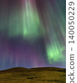 Vibrant aurora borealis dances across a starry night sky over rolling hills 140050229