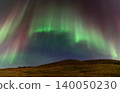 Vibrant green and pink aurora borealis dances across a starry night sky over a hill 140050230