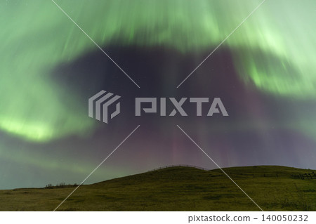 Vibrant green and purple aurora borealis dances across a starry night sky Vibrant green and purple aurora borealis dances across a starry night sky 140050232
