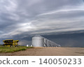 Agricultural grain silos stand under a dramatic, stormy sky with a farm implement nearby 140050233