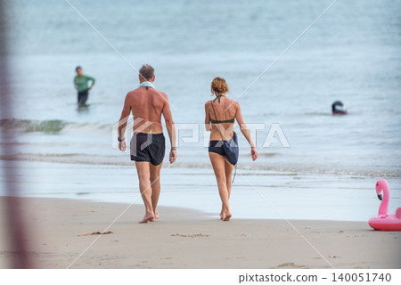 Couple walking barefoot along sandy beach near the shoreline enjoying relaxing seaside vacation calm ocean views leisure lifestyle Couple walking barefoot along sandy beach near the shoreline enjoying relaxing seaside vacation calm ocean views leisure lifestyle 140051740