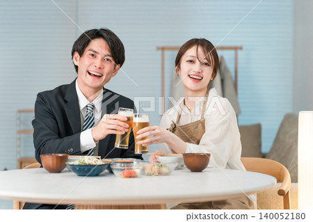 一對年輕的亞洲夫婦正在家裡的餐桌上吃喝。 140052180