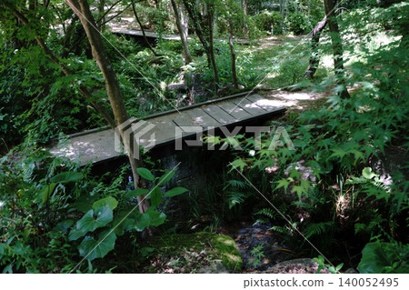 A stream and wooden bridge bathed in dappled sunlight. A stream and wooden bridge bathed in dappled sunlight. 140052495