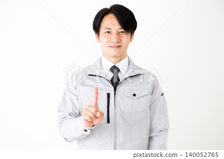 A middle-aged businessman in gray work clothes raises his index finger against a white background. A middle-aged businessman in gray work clothes raises his index finger against a white background. 140052765