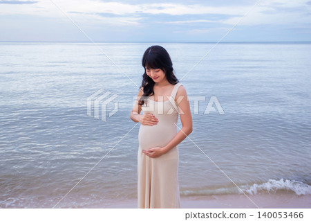 Pregnant woman standing on a beach with beautiful evening sea holding baby with love and care. Pregnant woman standing on a beach with beautiful evening sea holding baby with love and care. 140053466