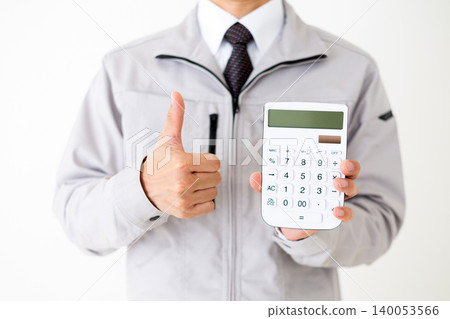 A middle-aged businessman in gray work clothes gives a thumbs-up while holding a white calculator against a white background. A middle-aged businessman in gray work clothes gives a thumbs-up while holding a white calculator against a white background. 140053566