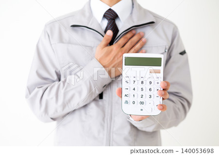 A middle-aged businessman in gray work clothes, holding a white calculator and placing his hand over his chest, against a white background. A middle-aged businessman in gray work clothes, holding a white calculator and placing his hand over his chest, against a white background. 140053698
