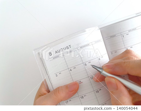 A woman's hand writing in her August schedule book. 140054044