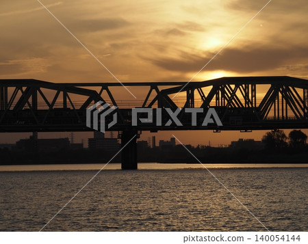 The silhouette of the JR Arakawa Railway Bridge against an orange sunset. The silhouette of the JR Arakawa Railway Bridge against an orange sunset. 140054144