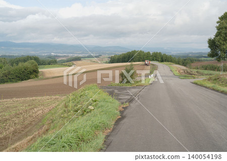 A red tractor driving along the hills of Biei, Hokkaido; the rural landscape of early autumn in September; Kamifurano A red tractor driving along the hills of Biei, Hokkaido; the rural landscape of early autumn in September; Kamifurano 140054198