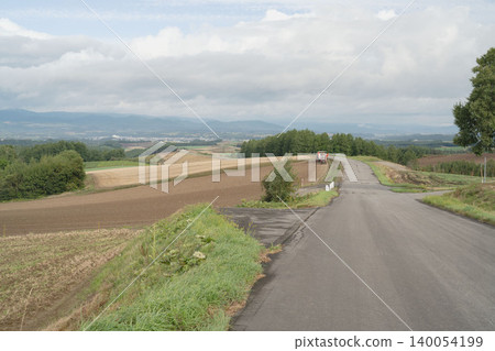 A scenic drive through the rolling hills of Biei, Hokkaido, and the sight of farm work, a panoramic view of early autumn fields in September. A scenic drive through the rolling hills of Biei, Hokkaido, and the sight of farm work, a panoramic view of early autumn fields in September. 140054199