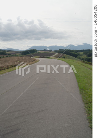 A vertical composition of the hills during a drive through Biei, Hokkaido, with the road and the Tokachi Mountain Range, and a panoramic view of the countryside in early autumn in September. A vertical composition of the hills during a drive through Biei, Hokkaido, with the road and the Tokachi Mountain Range, and a panoramic view of the countryside in early autumn in September. 140054206