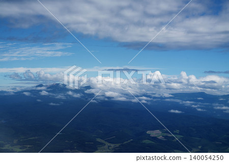 A panoramic view of mountain ranges and a sea of clouds over Hokkaido, against a clear blue sky, a stunning aerial view in the height of August, a bird's-eye view. A panoramic view of mountain ranges and a sea of clouds over Hokkaido, against a clear blue sky, a stunning aerial view in the height of August, a bird's-eye view. 140054250
