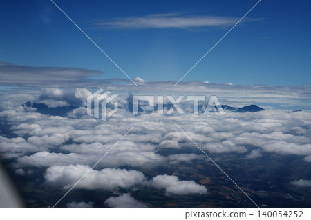 A panoramic aerial view of Hokkaido in mid-August, featuring a sea of clouds above, distant mountain ranges, and layers of fields. A panoramic aerial view of Hokkaido in mid-August, featuring a sea of clouds above, distant mountain ranges, and layers of fields. 140054252