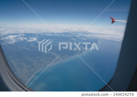 A breathtaking aerial view of Hokkaido from above, through the airplane window: the coastline and rice fields, the blue sea and the wing, a stunning scene in the height of August. A breathtaking aerial view of Hokkaido from above, through the airplane window: the coastline and rice fields, the blue sea and the wing, a stunning scene in the height of August. 140054259