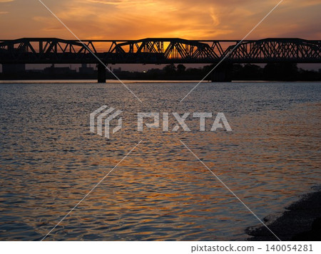 The silhouette of the Arakawa Railway Bridge against an orange sunset. The silhouette of the Arakawa Railway Bridge against an orange sunset. 140054281