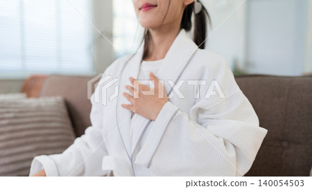 Asian women morning routine relaxation wellness moment touching chest hand on heart peaceful self care gratitude meditation at home living room white robe Asian women morning routine relaxation wellness moment touching chest hand on heart peaceful self care gratitude meditation at home living room white robe 140054503