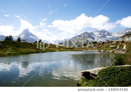 A stunning view of Zermatt in mid-August, with tourists and the Matterhorn in the distance from Leisee, Switzerland, amidst clouds and blue sky. A stunning view of Zermatt in mid-August, with tourists and the Matterhorn in the distance from Leisee, Switzerland, amidst clouds and blue sky. 140054590