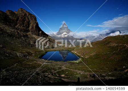 The Matterhorn and its reflection in Lake Riffelsee in Switzerland, hikers, and the breathtaking scenery of Zermatt in mid-August. 140054599