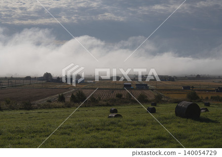 The misty countryside and mountain ranges of Hokkaido in the morning mist; a panoramic view of the early autumn morning mist in September; a tranquil rural landscape. 140054729