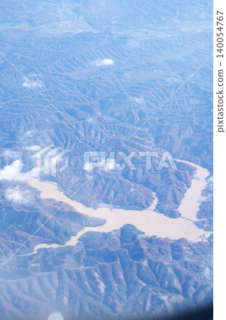 A stunning aerial view of a mountain dam lake and autumn-colored mountains from inside an aircraft, a beautiful scene from late October, in a vertical composition. A stunning aerial view of a mountain dam lake and autumn-colored mountains from inside an aircraft, a beautiful scene from late October, in a vertical composition. 140054767