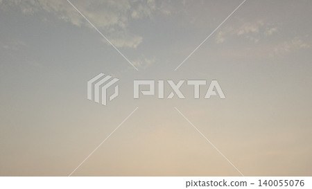 A soft-focus, minimalist photo of a sunrise sky with a warm gradient of muted blue, orange, and purple hues. A few wispy clouds and a tiny, distant object are visible. 140055076