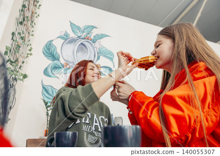 mother and daughter share a moment in a cafe. The mother has red hair and is wearing a green sweater. The daughter has long brown hair and is in an orange outfit. They are enjoying waffles together. mother and daughter share a moment in a cafe. The mother has red hair and is wearing a green sweater. The daughter has long brown hair and is in an orange outfit. They are enjoying waffles together. 140055307