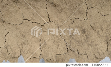 A close-up shot of dry, cracked, brownish earth or clay, featuring large, irregular fissures. The texture suggests a drought or arid environment. A close-up shot of dry, cracked, brownish earth or clay, featuring large, irregular fissures. The texture suggests a drought or arid environment. 140055355