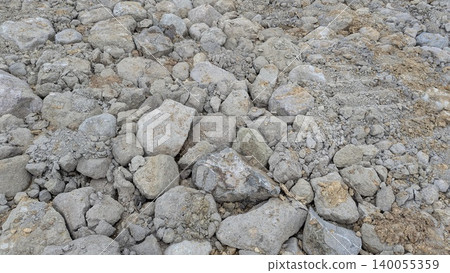 An extreme close-up of a pile of broken, irregular rocks gravel on a construction or geological site. The rough texture is dominated by shades of gray pale brown. An extreme close-up of a pile of broken, irregular rocks gravel on a construction or geological site. The rough texture is dominated by shades of gray pale brown. 140055359
