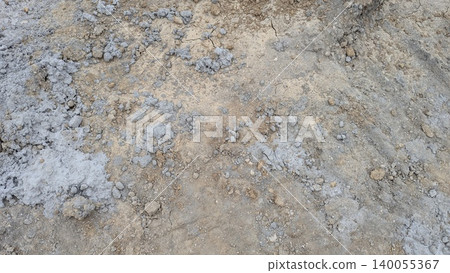 An extreme close-up of rough, textured earth showing a mixture of light brown gray soil gravel. The surface is uneven with dry, clumpy texture. 140055367