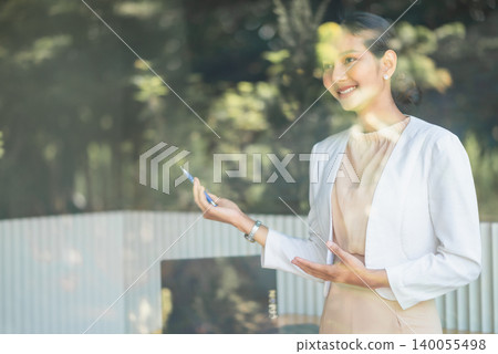 Smiling businesswoman in white blazer presenting with pen near laptop in bright office, using open gestures for corporate meeting, strategy planning, professional communication, and teamwork success. Smiling businesswoman in white blazer presenting with pen near laptop in bright office, using open gestures for corporate meeting, strategy planning, professional communication, and teamwork success. 140055498