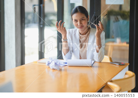 Frustrated businesswoman holding eyeglasses with crumpled paper and sales documents on office table, showing work stress, business failure, deadline pressure, problem solving, Frustrated businesswoman holding eyeglasses with crumpled paper and sales documents on office table, showing work stress, business failure, deadline pressure, problem solving, 140055553