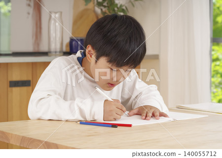 一個男孩在燈光明亮的客廳裡做作業。 一個男孩在燈光明亮的客廳裡做作業。 140055712