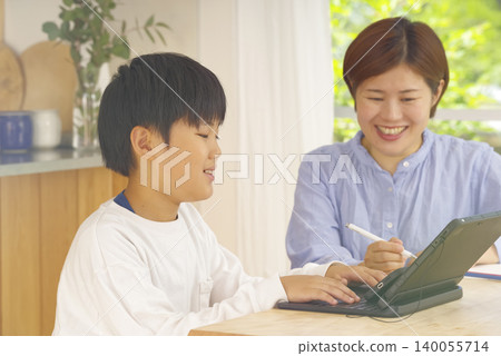 A boy studying on a tablet, watched over by his mother. A boy studying on a tablet, watched over by his mother. 140055714