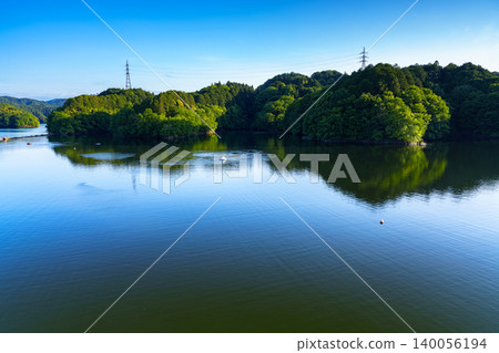Early summer at Nunome Dam; the silence before sunset; the green of the opposite shore sandwiched between the blue sky and the blue sky reflected on the lake's surface. Early summer at Nunome Dam; the silence before sunset; the green of the opposite shore sandwiched between the blue sky and the blue sky reflected on the lake's surface. 140056194