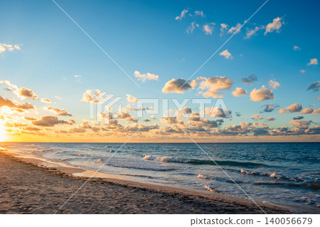 Sunset at the beach with calm waves and fluffy clouds in the sky Sunset at the beach with calm waves and fluffy clouds in the sky 140056679