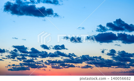 Colorful sunset sky with scattered clouds over a horizon at dusk near a tranquil landscape 140056682